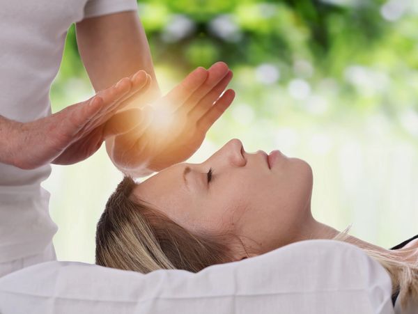 Reiki practitioners hands radiating light over a woman's head as she is lying down with eyes closed