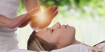 Women laying down.  Reiki practitioner's hands with white light orb
