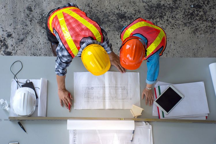 Two construction workers examining blueprints at a work table.