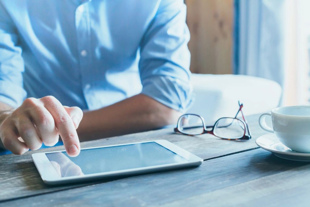 Person utilisant une tablette près de lunettes et d'une tasse de café.
