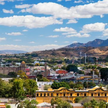 Cityscape with mountains under a blue sky filled with clouds.