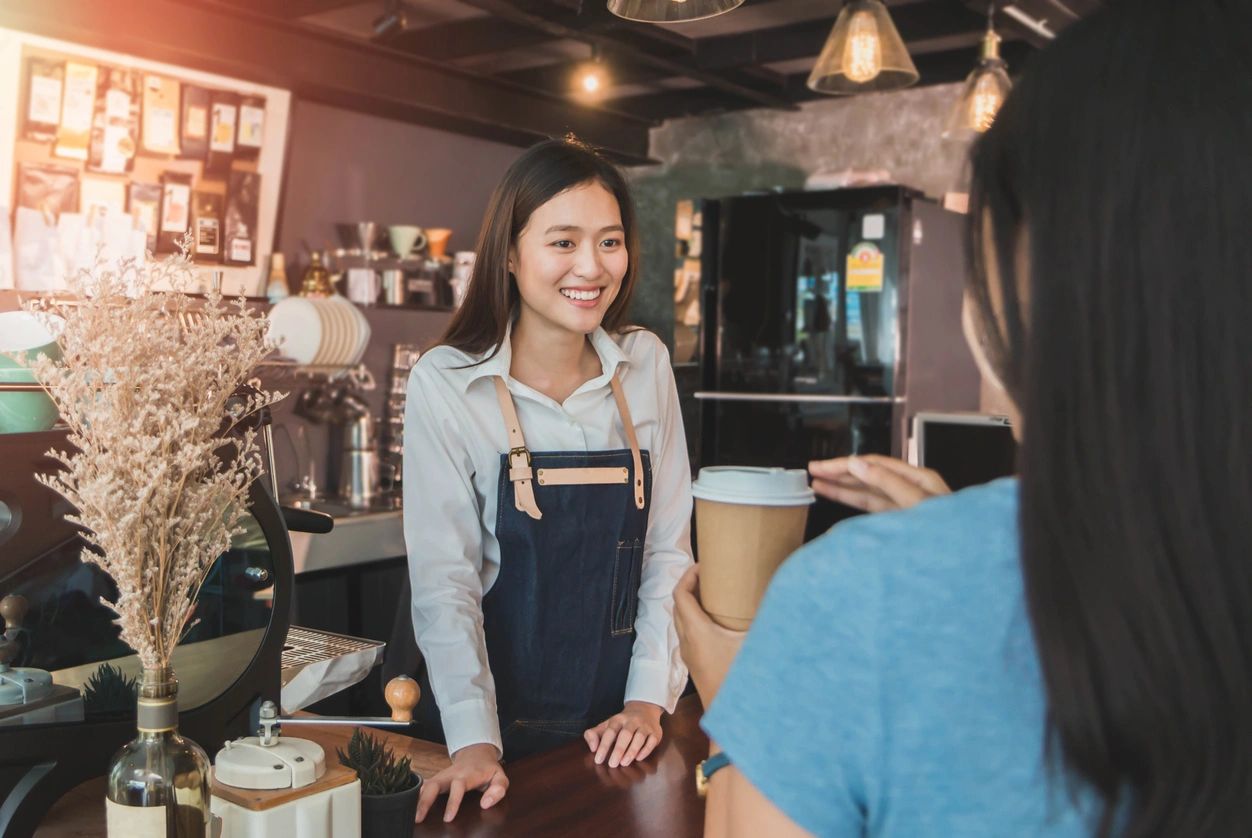 A server issues the cup of coffee to the customer with a smile.