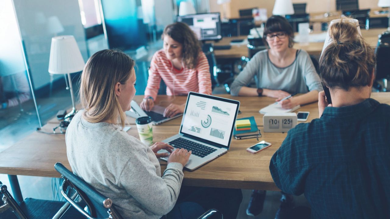 Group of professionals collaborating in a modern workspace, analyzing data on a laptop, discussing market trends, and strategizing for business growth.