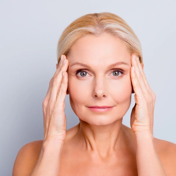 Mature woman gently touching her temples, looking calm and serene.