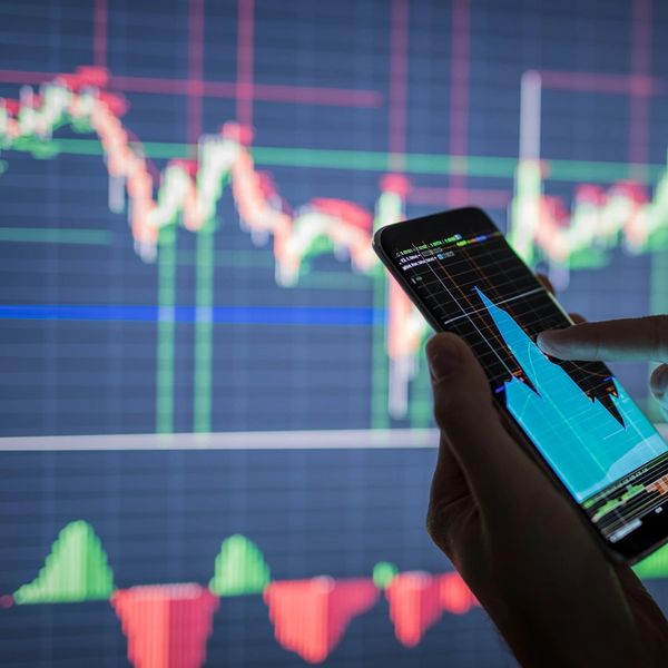 Person analyzing stock market charts on smartphone and screen.