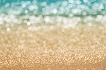 Close-up of sparkling sand with blurred ocean in the background.