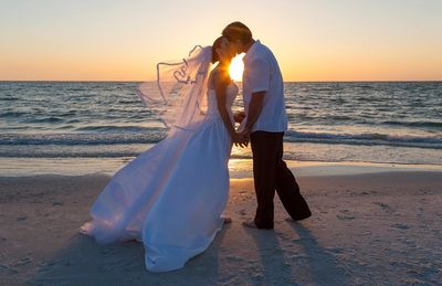 Bride and groom sharing a sunset kiss on the beach.
