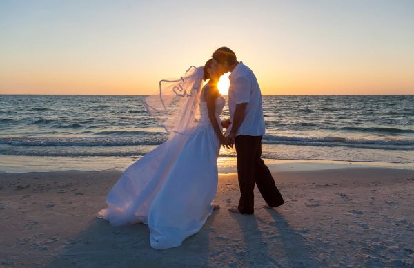 Bride and groom kissing on the beach at sunset.