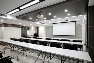 Modern conference room with rows of tables and a projector screen.