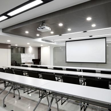 Modern conference room with white tables, black chairs, and a projector screen.