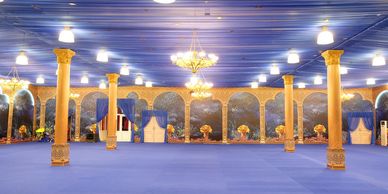 Lavish hall with golden columns and blue decor illuminated by chandeliers.