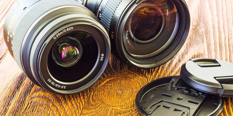 Two camera lenses and a lens cap on a wooden surface.