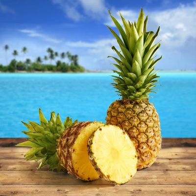 Fresh pineapples on a wooden table with a tropical ocean backdrop.