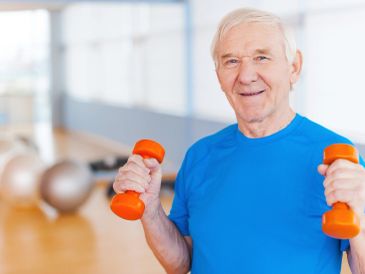 Elderly man lifting orange dumbbells in a gym.