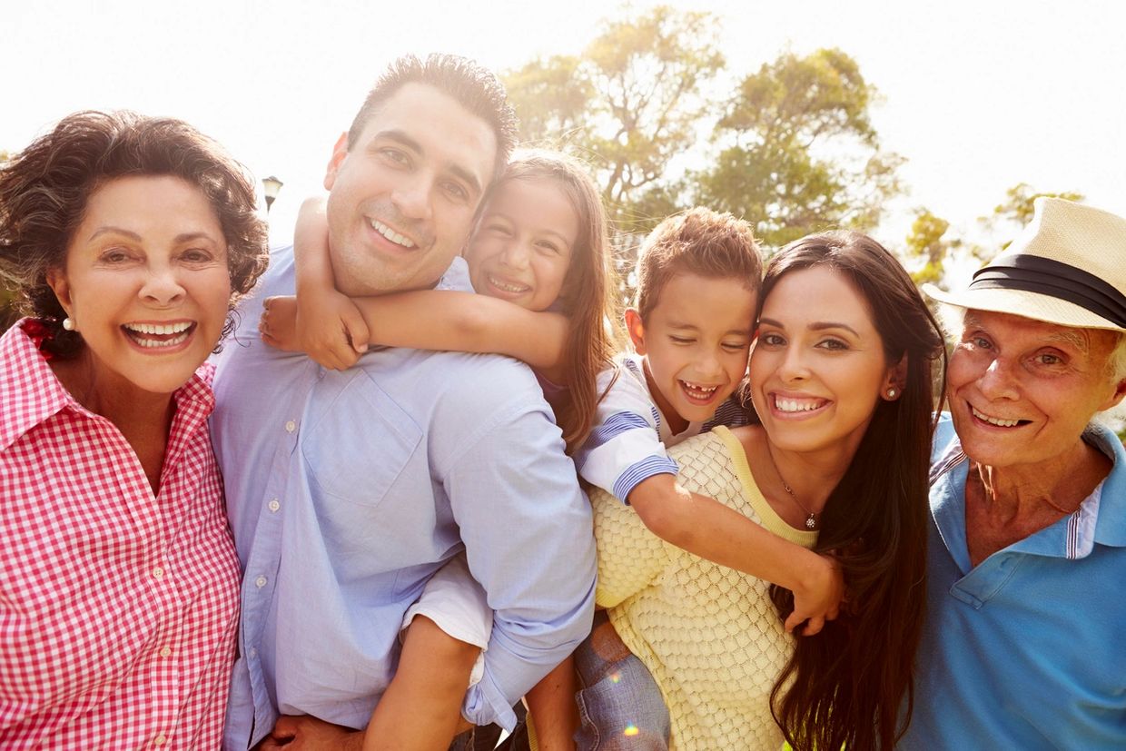 A joyful multi-generational family posing happily outdoors in the sunlight.