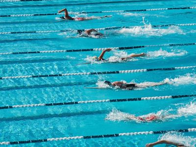Swimmers racing in an outdoor pool with clear blue water.