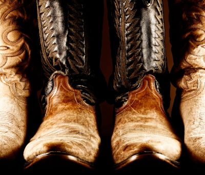 Close-up of three worn leather cowboy boots with intricate stitching.