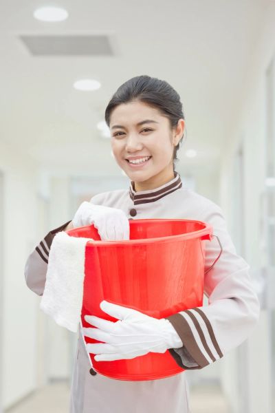 Smiling cleaning staff holding a red bucket and cloth.