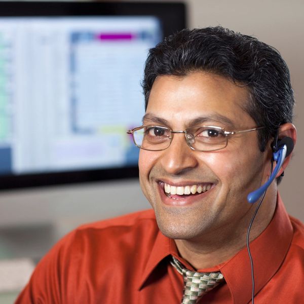 Smiling man with glasses and headset in an office setting.