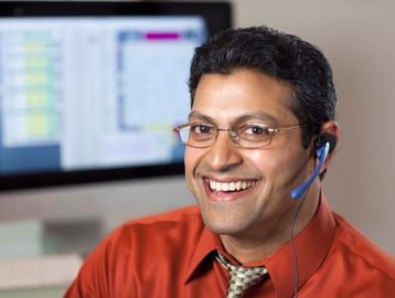 Man wearing headset smiles in an office setting.