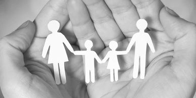 Paper cutout family held in caring hands.