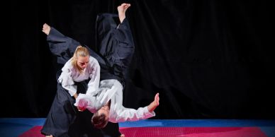 Two martial artists in white uniforms performing a dynamic throw on a mat.