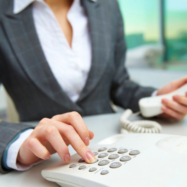 Person dialing a number on a white office phone.