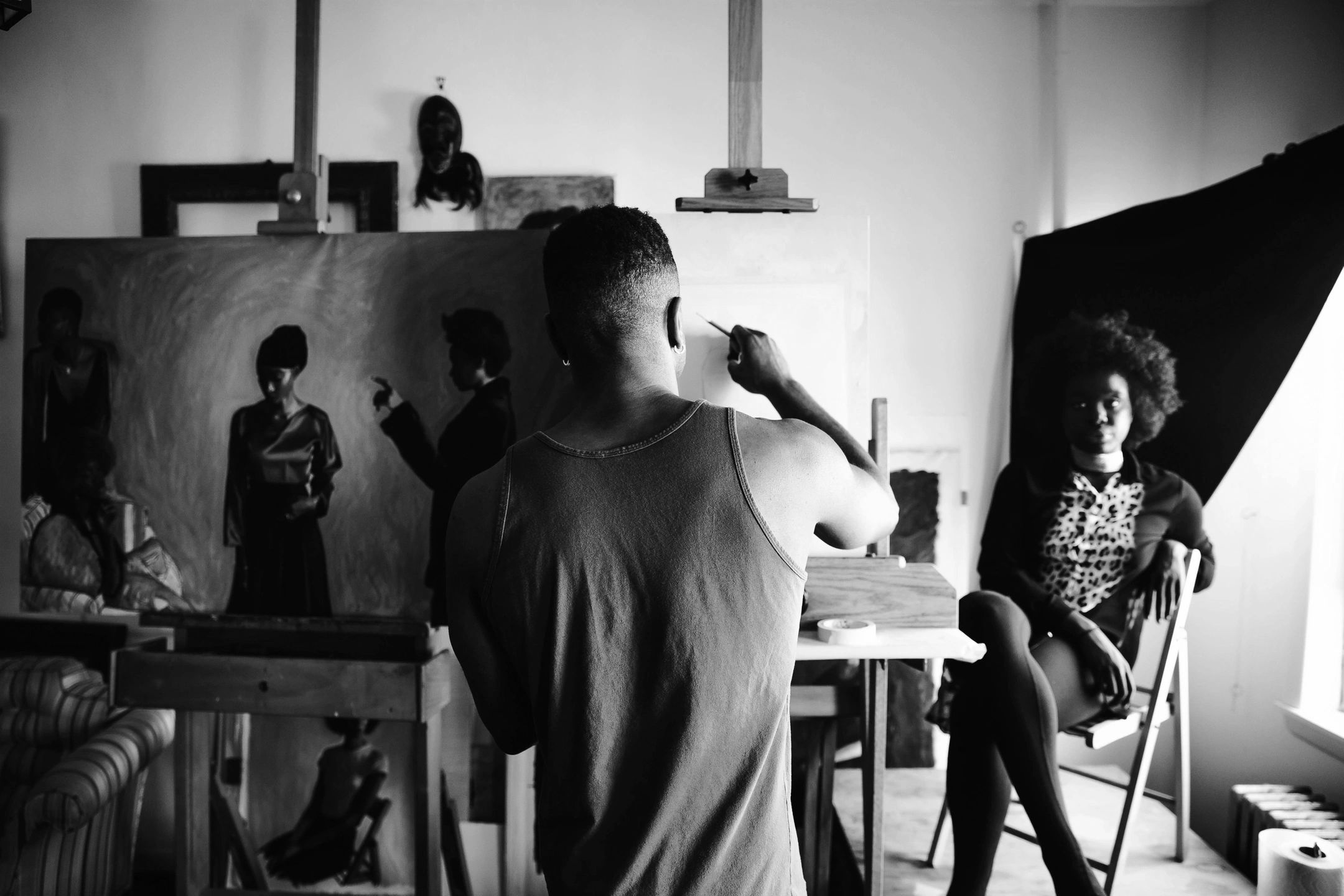 Artist painting a portrait of a seated woman in a studio.