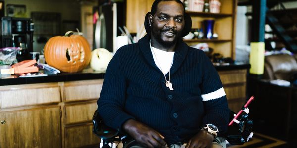 An African American man sitting in a wheelchair in his home and smiling.