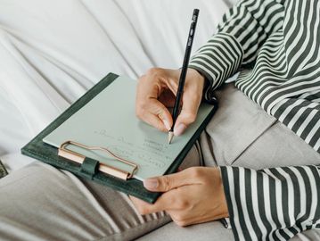A woman is writing on a notepad while lying in bed. 