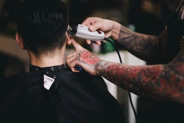Tattooed barber giving a haircut with clippers.