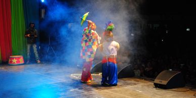 Two clowns performing on a smoky stage with colorful costumes.