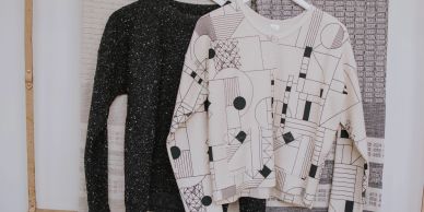 Two sweaters hanging side by side, one black and one white with a geometric pattern.