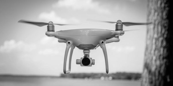A white Phantom drone flying near a tree over water on a clear day.