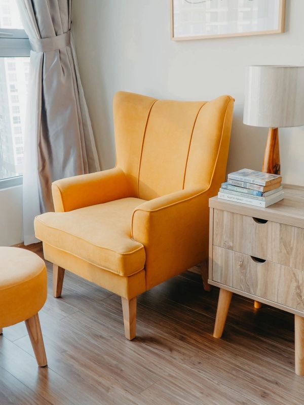 Cozy yellow armchair with wooden legs in a bright living room corner.