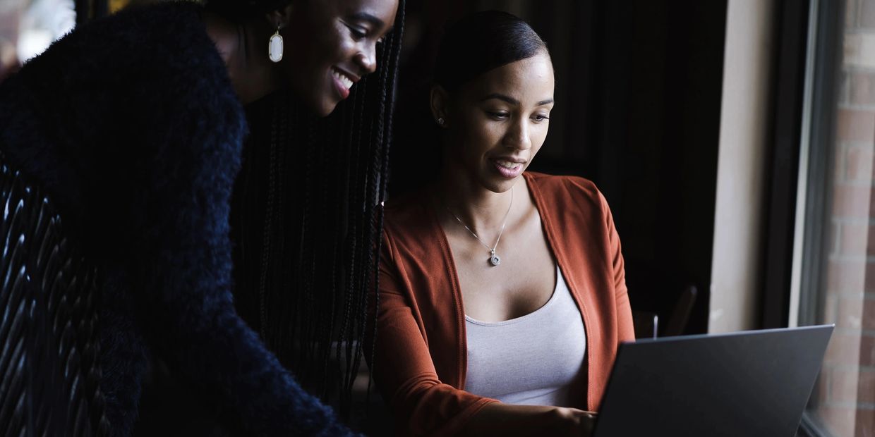 A woman watching digital media on another woman's laptop