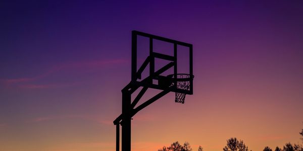 Silhouette of a basketball hoop against a colorful sunset sky.