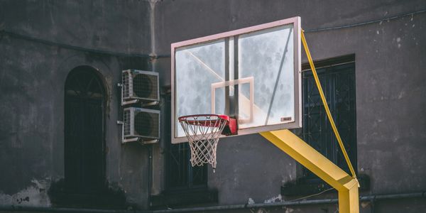 Outdoor basketball hoop with a transparent backboard and yellow pole.
