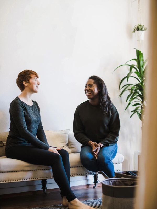 Two women happily chatting on a couch indoors.