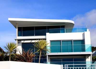 Modern white house with blue glass balconies under a clear sky.