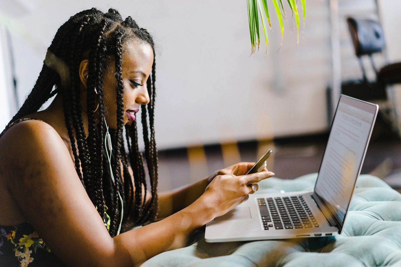 Woman with braided hair using a smartphone while working on a laptop, illustrating personalized mobile advertising strategies and user engagement.