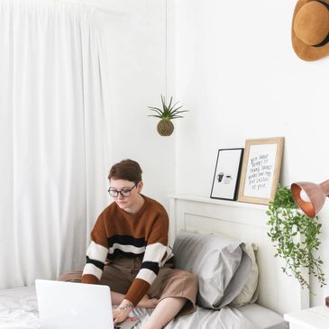 Person working on a laptop in a cozy, minimalist bedroom.