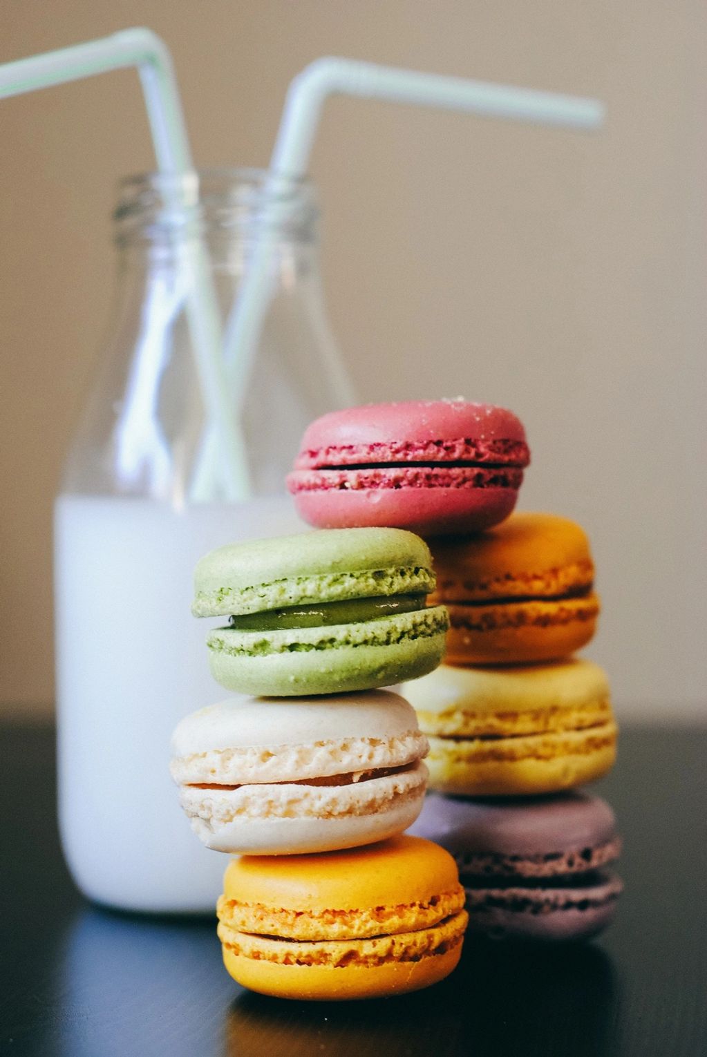 Colorful macarons stacked beside a glass bottle of milk with two straws.