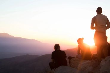 Three people enjoying a mountain sunset.