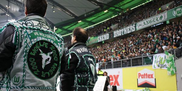 Fans wearing VfL Wolfsburg-themed jackets at a crowded stadium.
