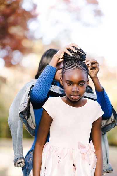A woman braiding a young girl's hair outdoors.