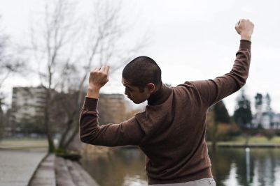 Person stretching arms outdoors near water and trees.