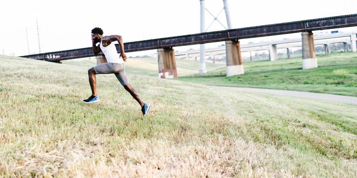 A runner powers uphill, showcasing strength and endurance against a backdrop of bridges and fields.