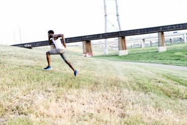 Man running uphill outdoors near a bridge.