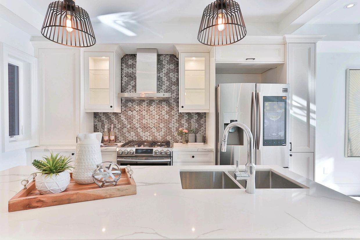 Modern white kitchen with marble island and floral backsplash.